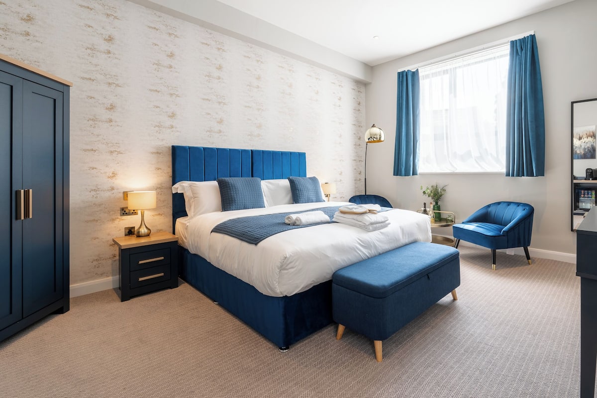 A modern bedroom with a large bed, a nightstand, a chair, and a wardrobe.