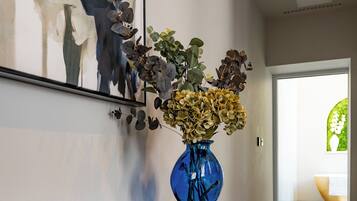 Um corredor com uma mesa consola escura, um vaso azul com flores e uma grande pintura abstrata na parede.