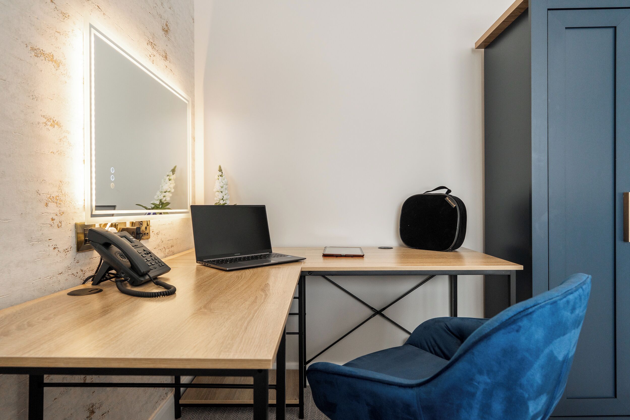 Een moderne kantoorruimte met een houten bureau, een laptop, een zwarte telefoon, een blauwe stoel en een blauwe kast.