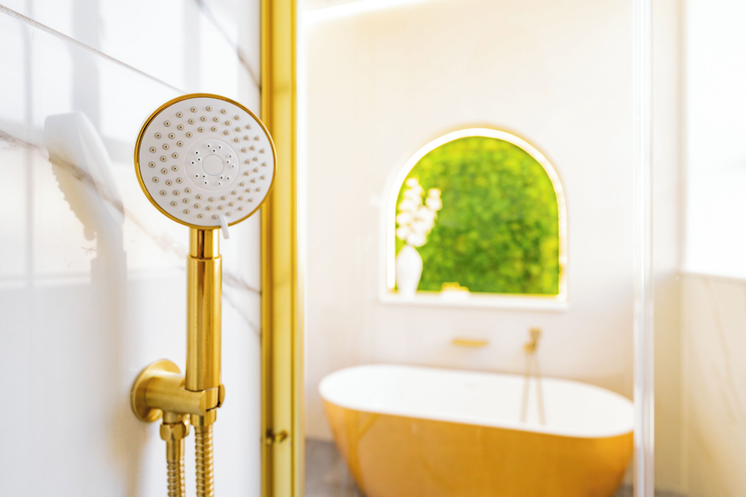 Un baño con ducha y bañera doradas, y una ventana con vistas verdes.