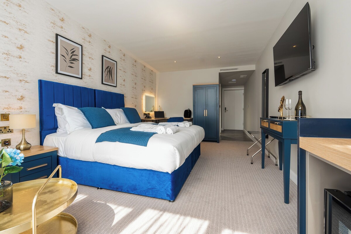 A modern hotel room with a large bed, a desk, a flat-screen TV, and a wardrobe.