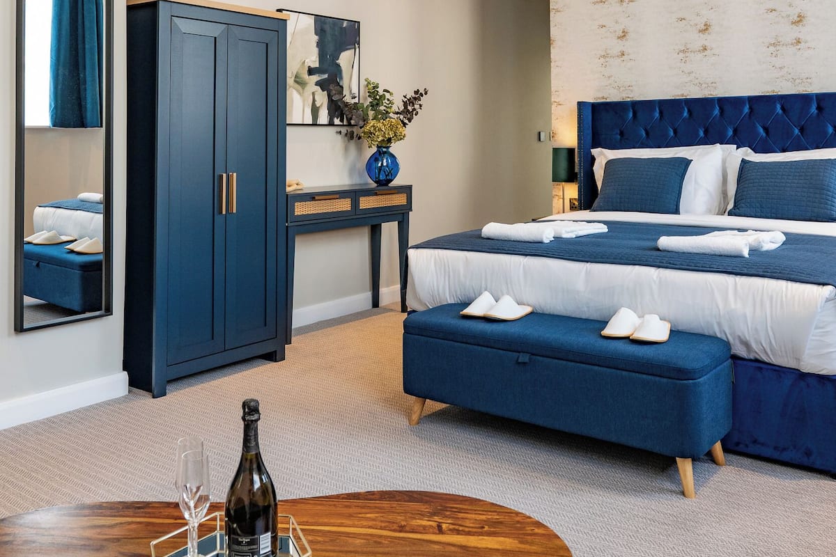 A modern hotel room with a large bed, a wardrobe, a desk, and a round coffee table.