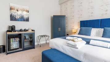 Una habitación de hotel con cama, minibar, escritorio y una máquina de café, además de una obra de arte colgada en la pared.