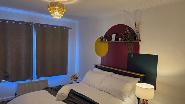 Un dormitori modern amb llit, taula de nit, làmpada i una decoració mural.