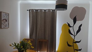 Una habitació amb taula de menjador, cadires, cortina, làmpada de paret i quadre amb marc.