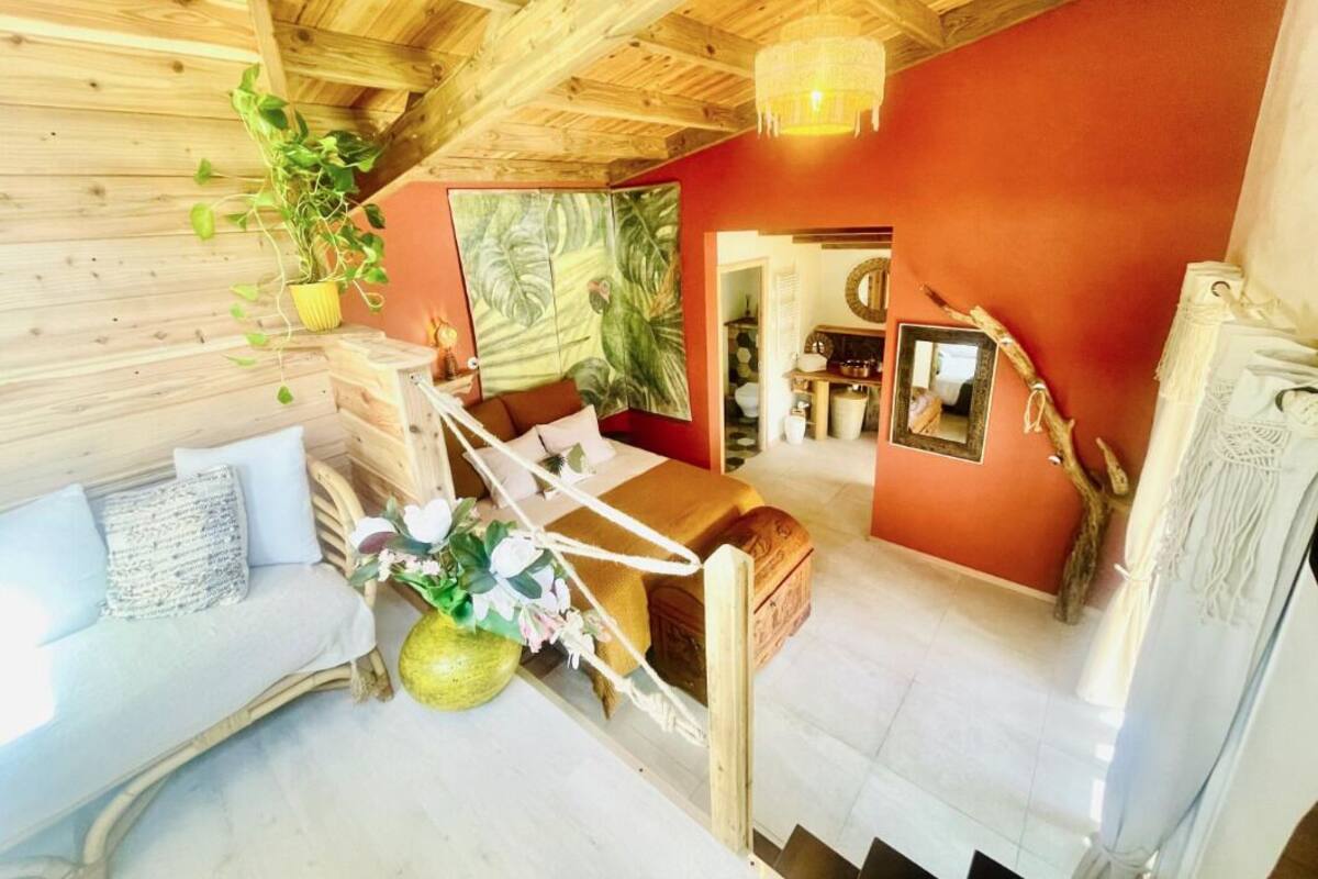 A cozy room with a wooden ceiling, a red accent wall, a wooden bed, a white sofa, and a dining area with a table and chairs.