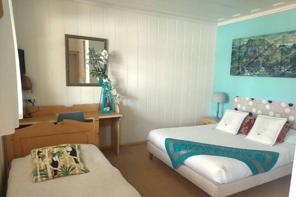 A bedroom with a bed, a desk, a chair, a mirror, and a painting on the wall.
