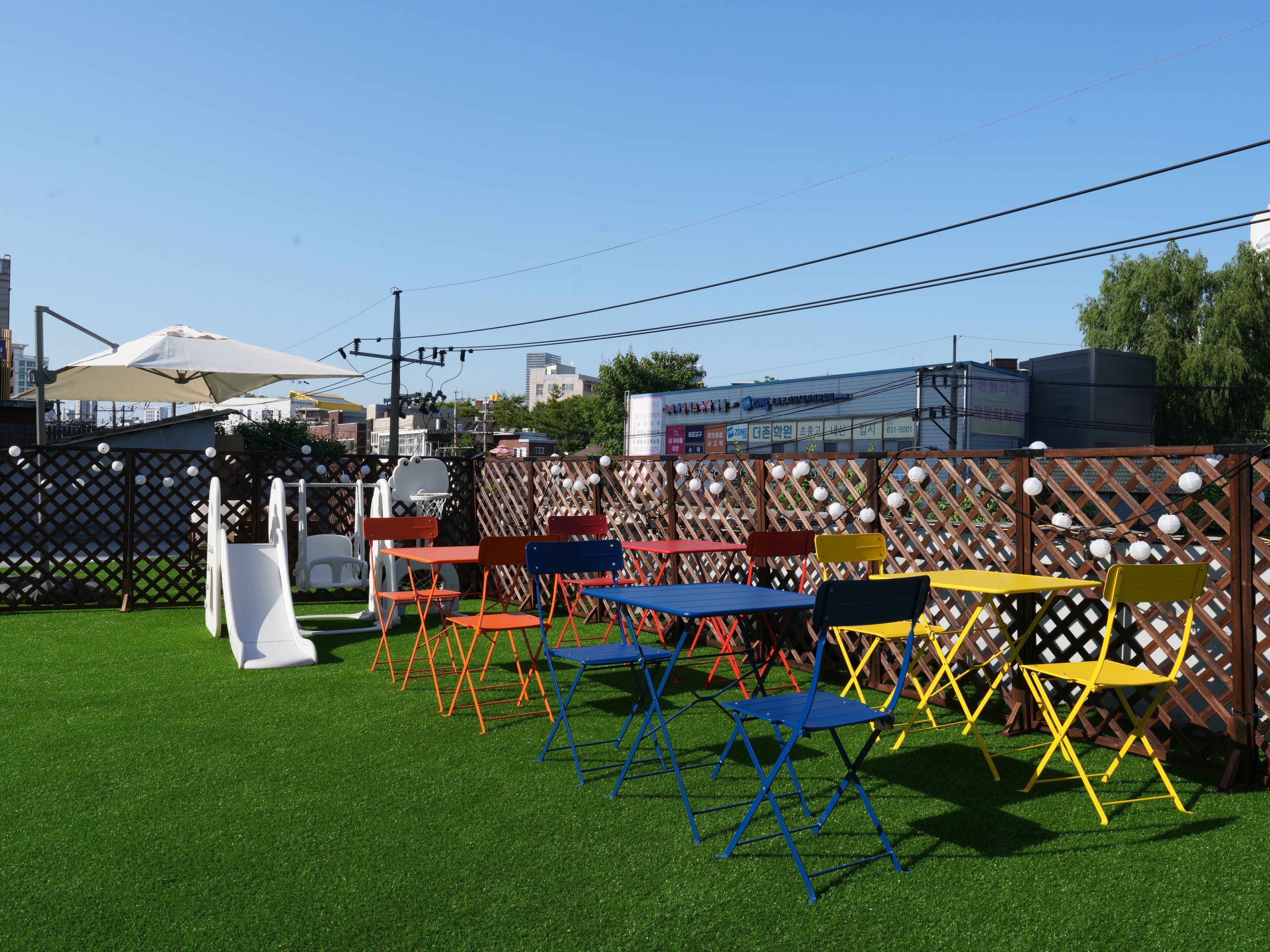 An outdoor seating area with colorful chairs and tables, a fenced area, and a building in the background.