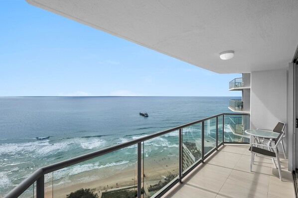 A balcony with a view of the ocean, a ship in the distance, and a beach with people.