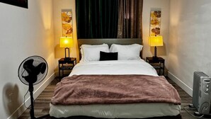 A hotel room with a bed, two bedside lamps, a heater, and a fan. - Gateway to Serenity-welcome Home (London)