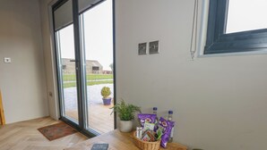 Una habitación moderna con una mesa de madera, un sofá verde, una planta en maceta y una ventana con vistas a un edificio y un jardín.