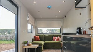 Un espacio habitable compacto con sofá, una mesita, zona de cocina y vistas al exterior.