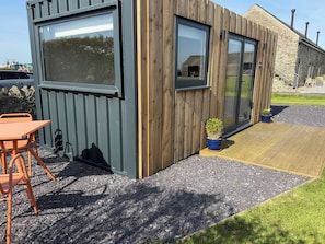 A modern building with large windows, a wooden exterior, and a small outdoor seating area with a table and chairs. - Caban (Ty Croes)
