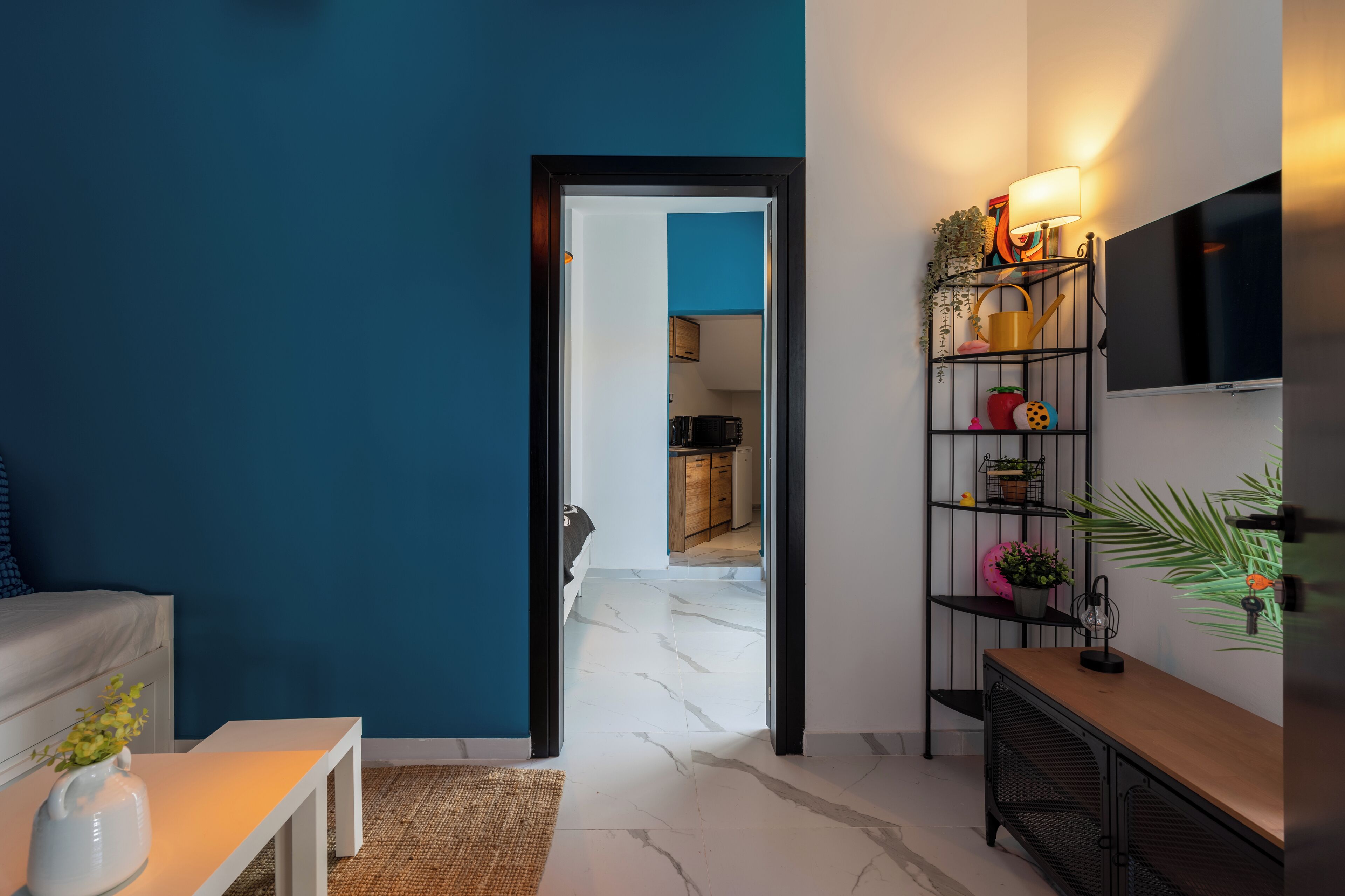 Una sala de estar moderna con una pared azul destacada, un sofá blanco, una mesa de centro con un florero y un televisor montado en la pared.