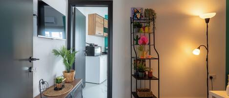 A modern kitchen with a microwave, toaster, and sink. There is a plant shelf with various plants and a floor lamp.