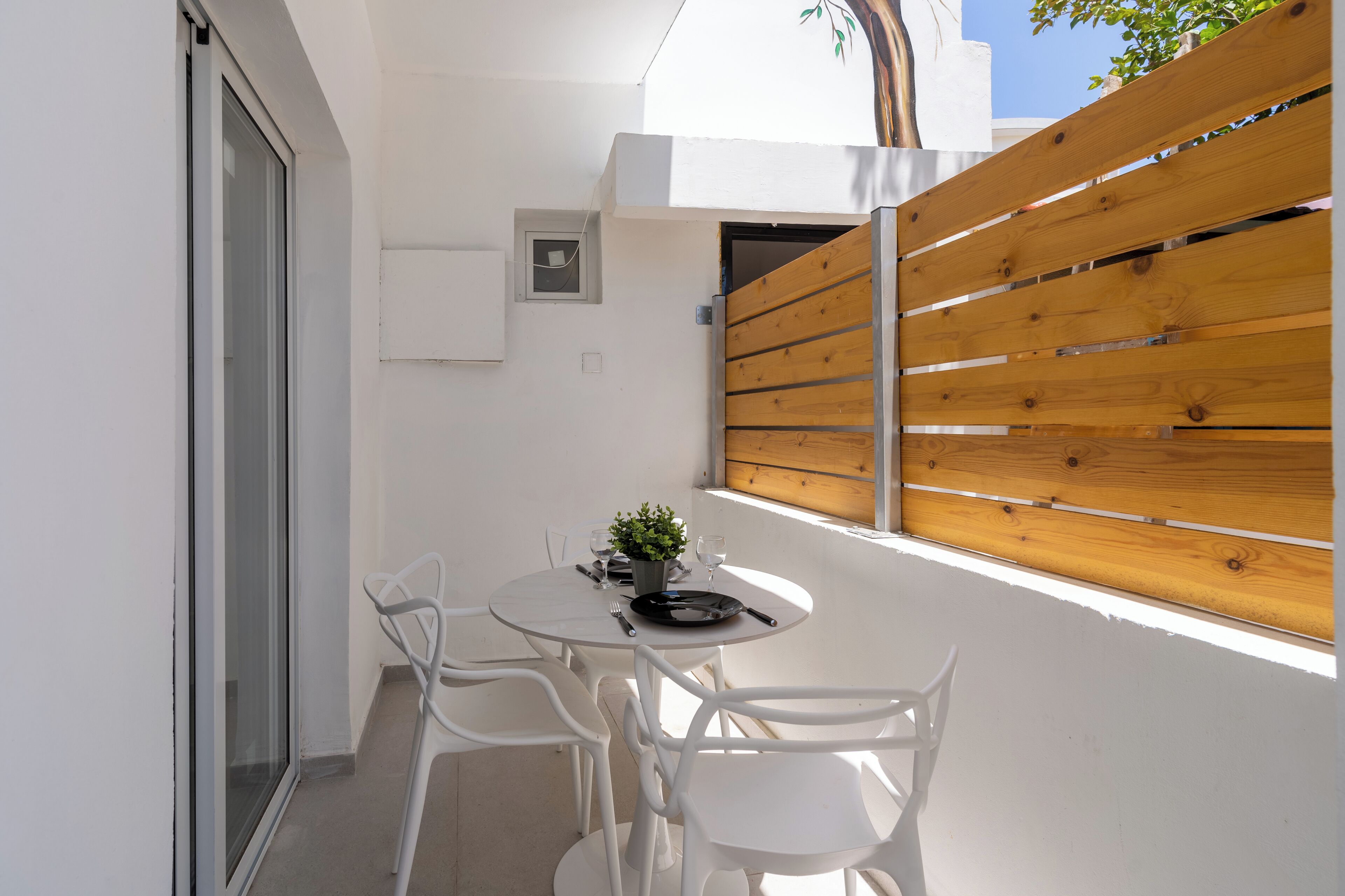 A small outdoor dining area with a round table, white chairs, and a wooden fence.