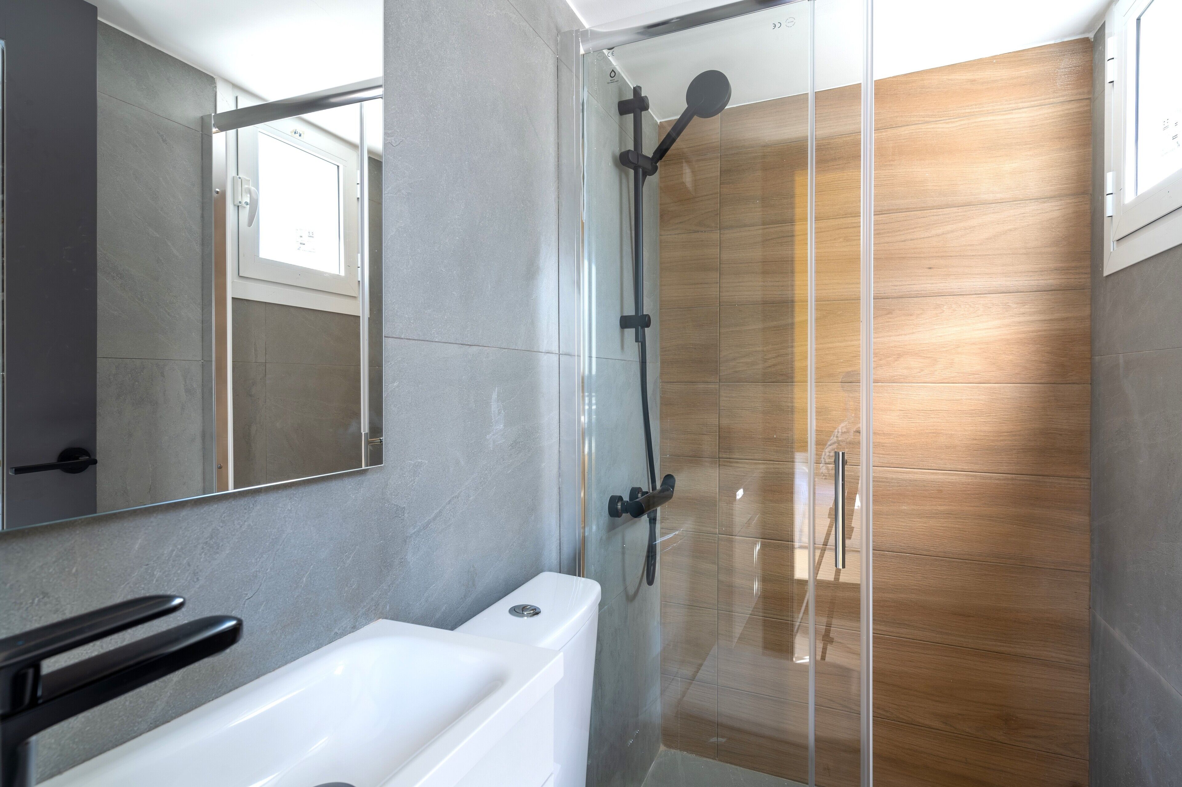 A modern bathroom with a glass-enclosed shower, a white bathtub, and a large mirror.
