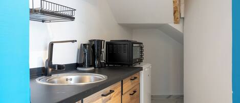 A compact kitchen with a sink, wooden cabinets, and a black countertop.