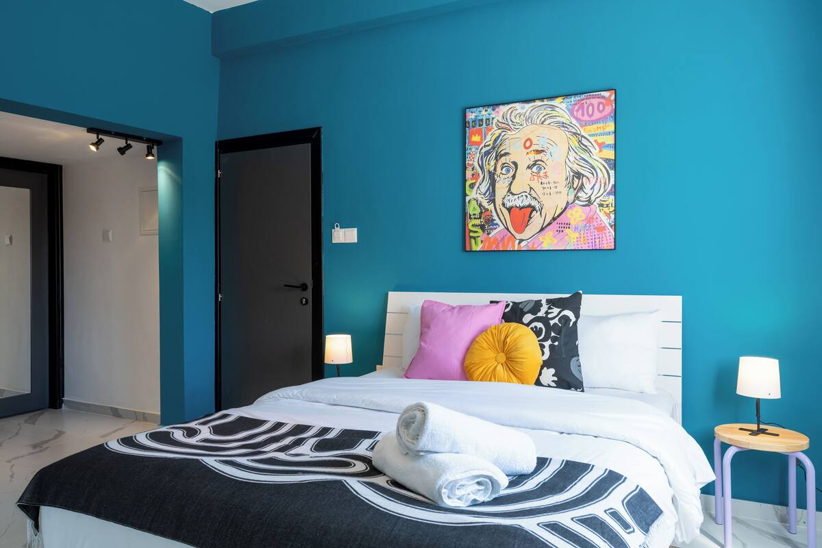 Un dormitorio moderno con una pared verde aguamarina, una cama grande con colcha estampada en blanco y negro, y un cuadro de arte pop colorido sobre la cama.