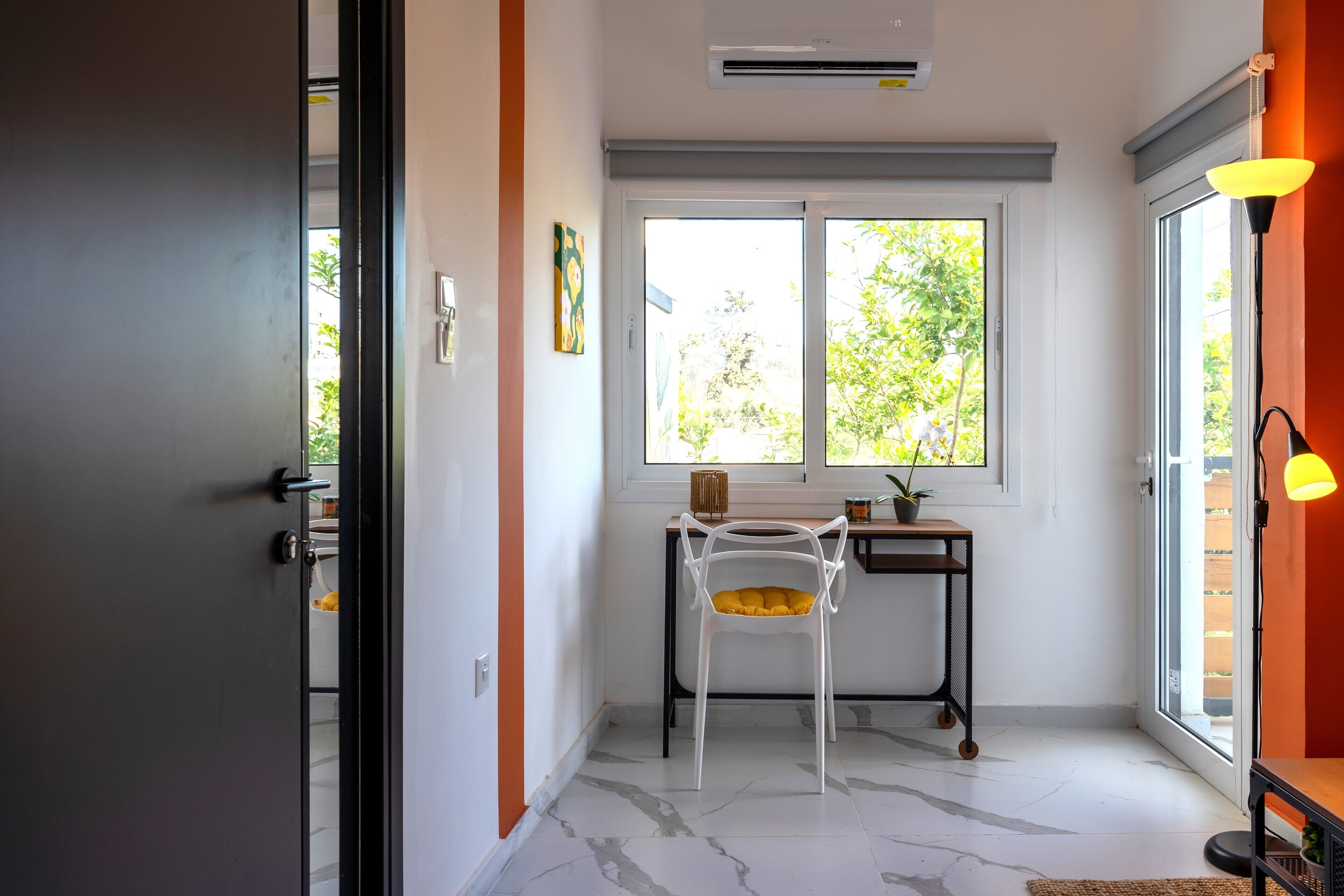 A modern room with a large window, a desk, a chair, and a lamp.