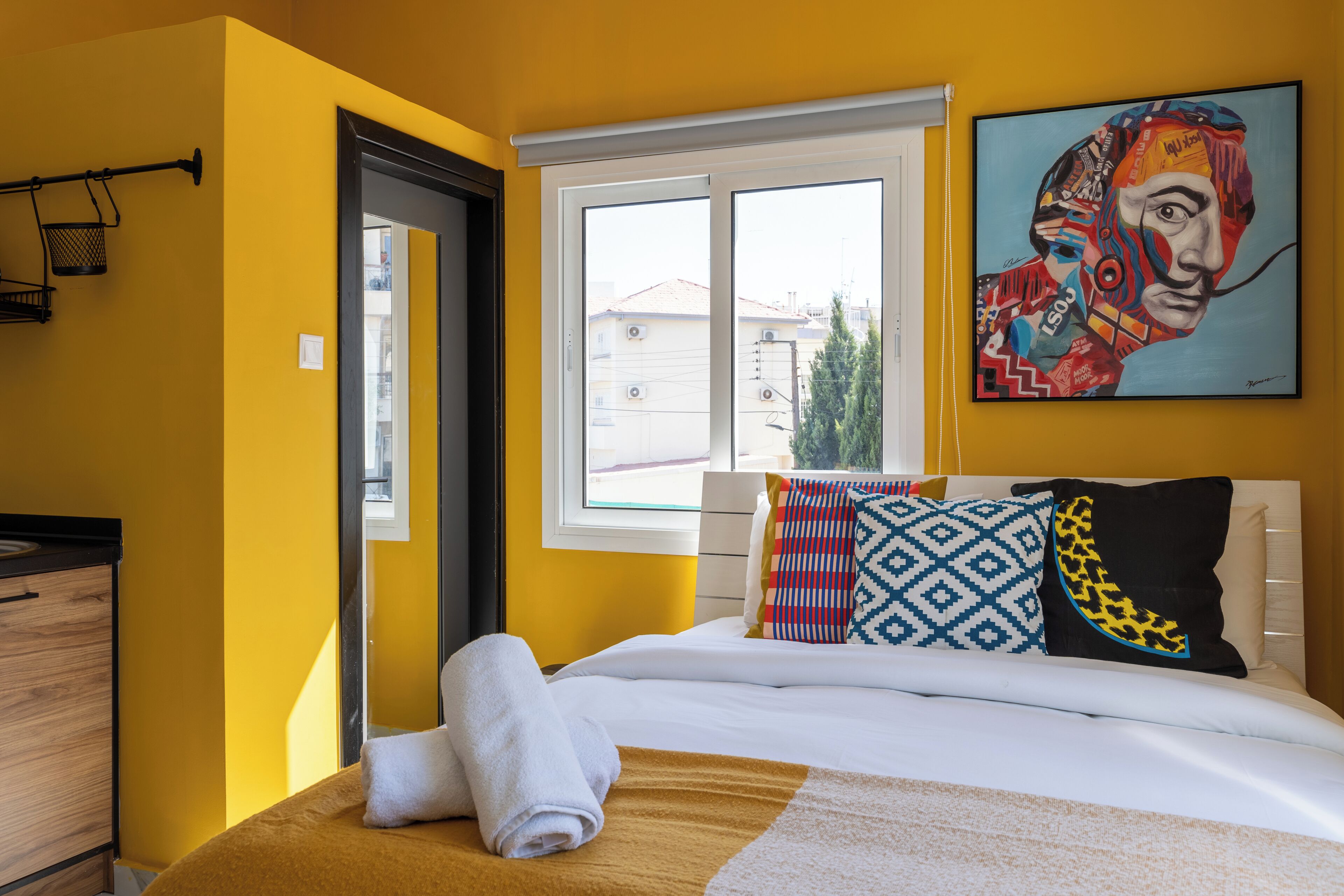 Una habitación de hotel con cama, ventana, un cuadro y una puerta.