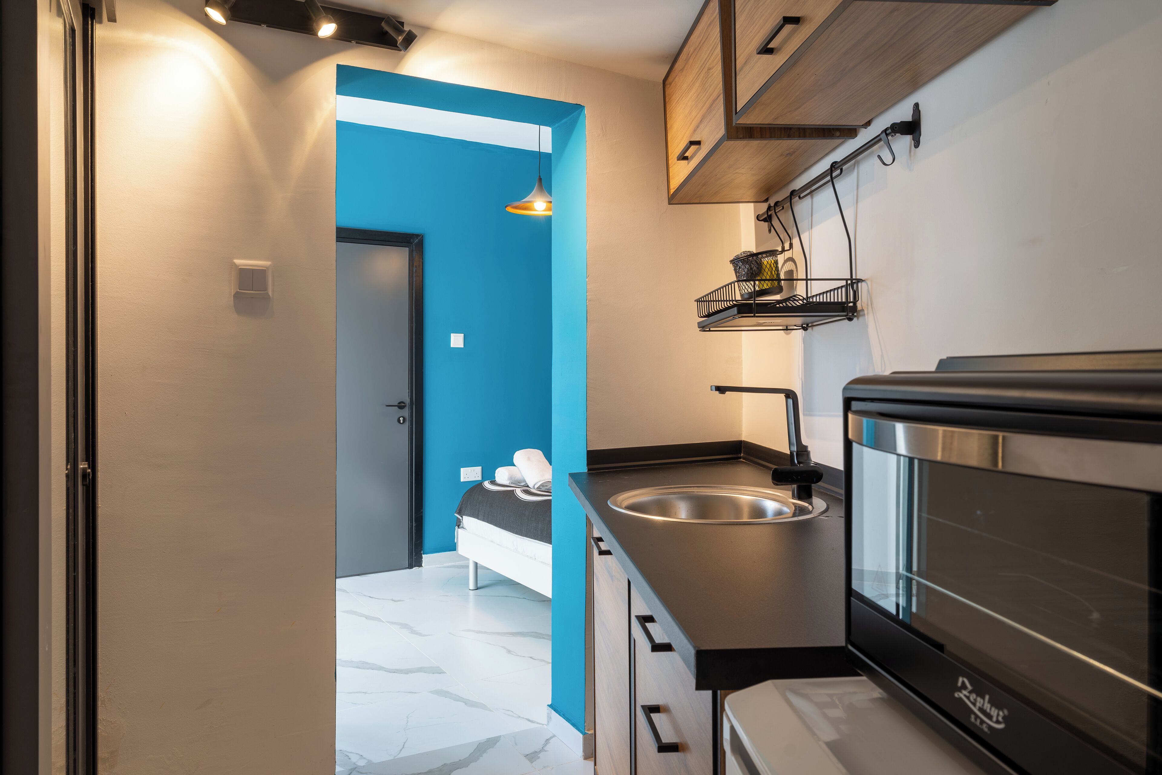 A compact kitchen with a modern design, featuring a built-in oven, a sink, and a hanging rack.