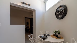Ein Essbereich mit einem runden Tisch, weißen Stühlen, einer Wanduhr und einem kleinen Blumentopf.