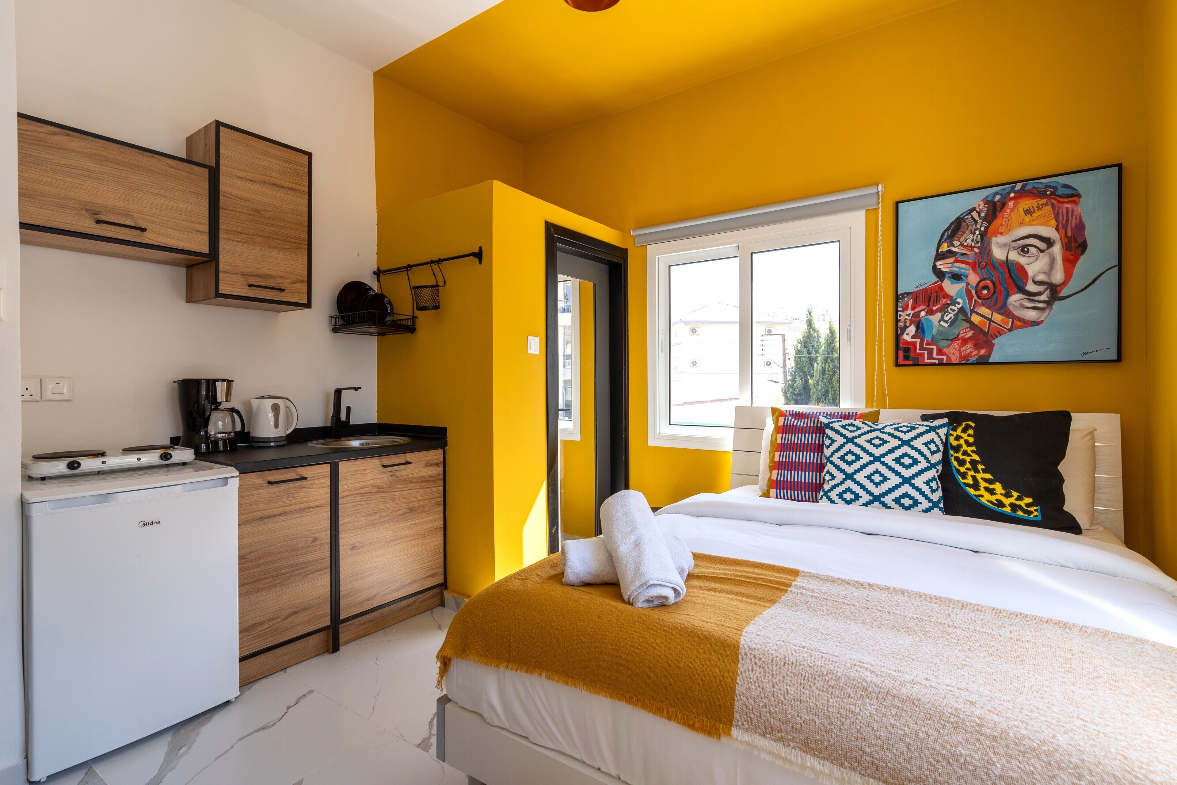 Una habitación de hotel compacta con una cama, una kitchenette pequeña y una ventana con vistas a la ciudad.