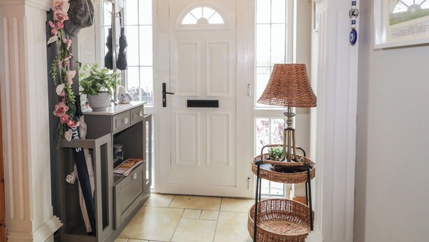A hallway with a white door, a wicker lamp, and a wall-mounted shelf with decorative items. - Donagh Cross Town House (Carndonagh)