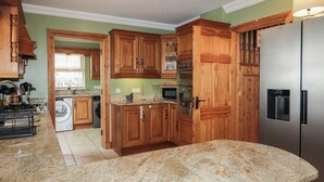 A kitchen with wooden cabinets, granite countertops, a stainless steel refrigerator, and a built-in oven. - Donagh Cross Town House (Carndonagh)