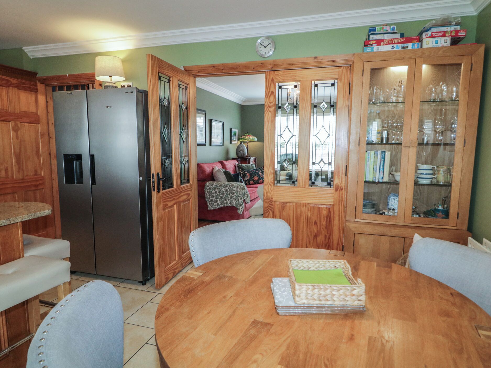 A dining area with a wooden table, chairs, a refrigerator, and a cabinet with glass doors.
