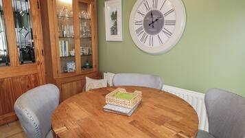 Une table ronde en bois, sur laquelle sont posés un panier tressé et un tableau encadré, entourée de chaises grises recouvertes de tissu.