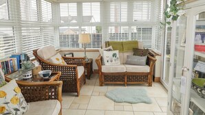 A cozy living room with wicker furniture, a glass cabinet, and a view through large windows. - Donagh Cross Town House (Carndonagh)
