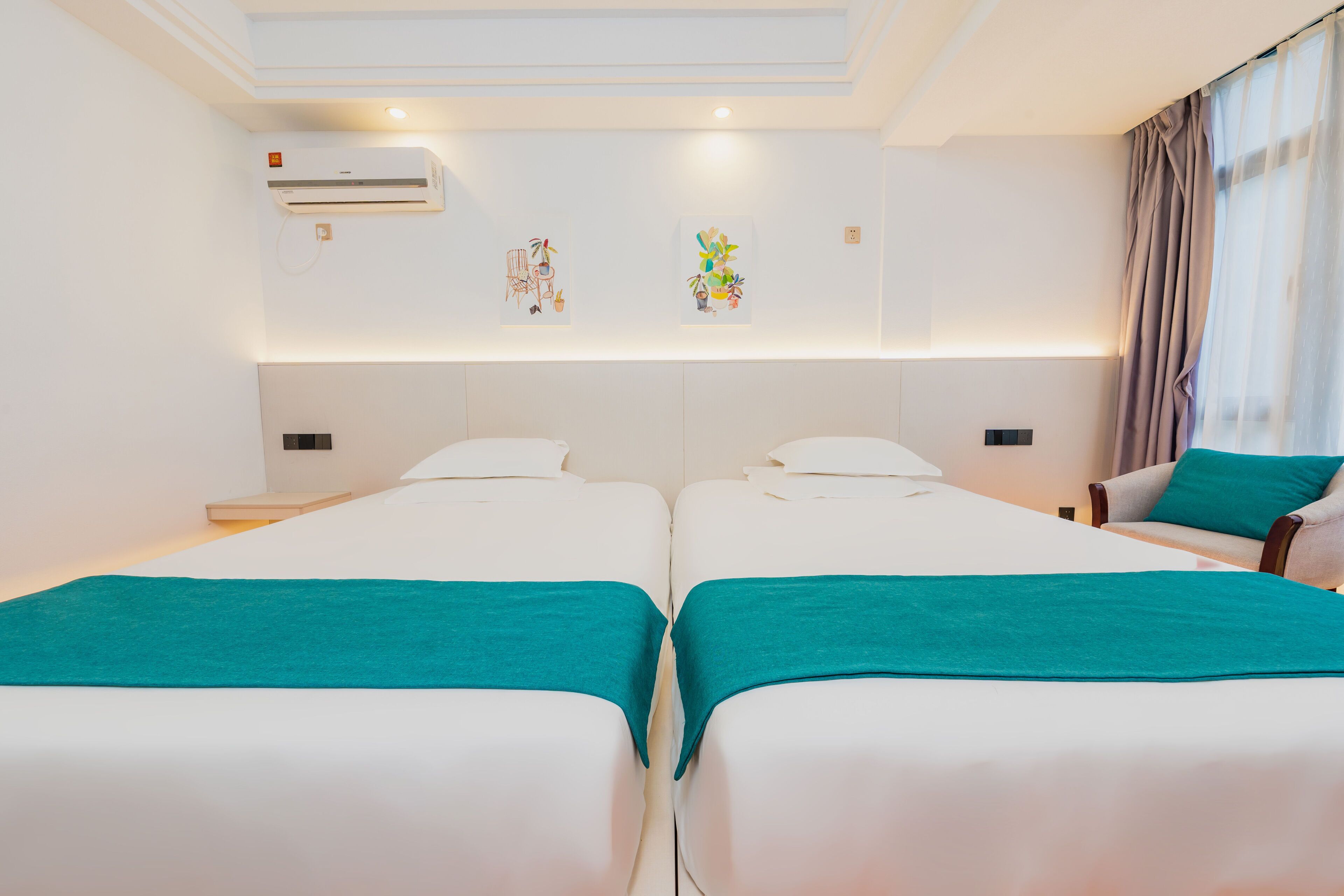A hotel room with two beds, a chair, a desk, and an air conditioning unit.