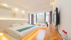 Una habitación de hotel moderna con una cama grande, suelo de madera, una mesa de comedor con fruta y un televisor en la pared.