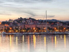Un paisaje urbano frente al mar, con edificios, una torre destacada y un puerto deportivo con barcos.