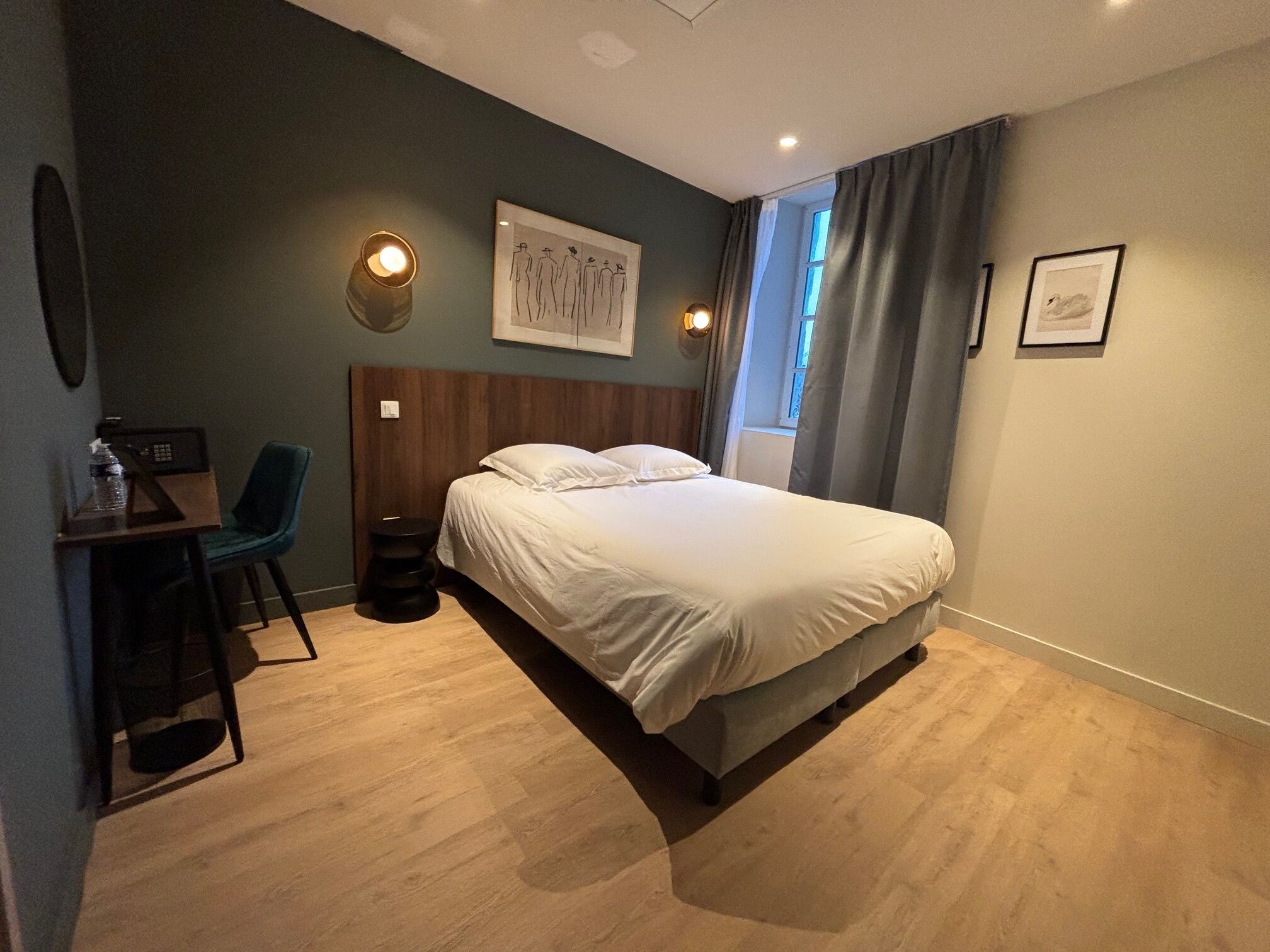 Habitación de hotel con cama, escritorio con silla, una mesita y una lámpara de pared.