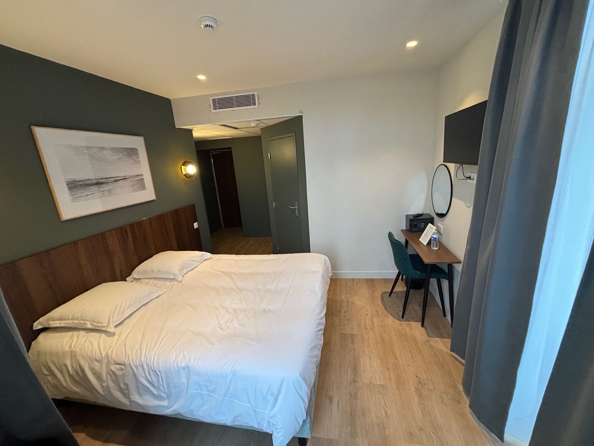 Habitación de hotel con cama, escritorio, silla, espejo y un cuadro en la pared.