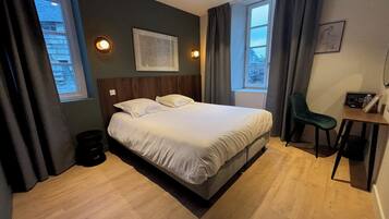 Quarto de hotel com uma cama grande, uma escrivaninha e duas janelas.