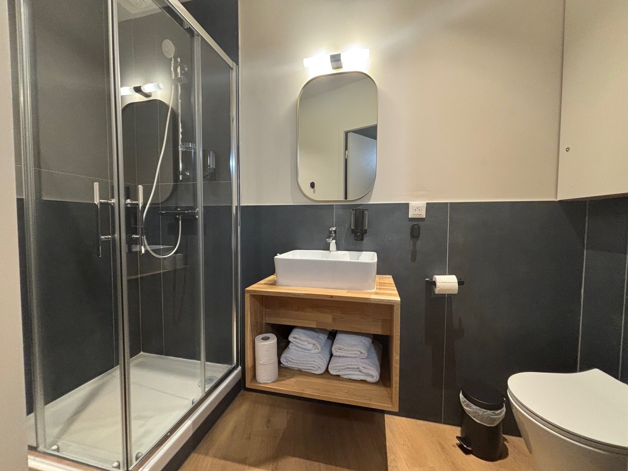 Une salle de bain moderne avec une douche à parois de verre, un meuble-lavabo en bois avec un évier, un miroir et des toilettes.