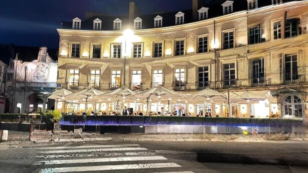 Un bâtiment historique doté d’une terrasse de café, de grandes fenêtres et d’une fontaine.