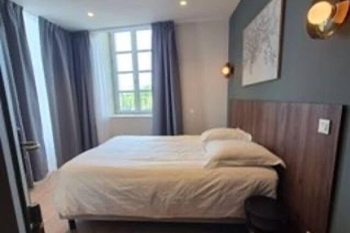 A bedroom with a bed, a window with curtains, a wall-mounted light, and a wooden floor.