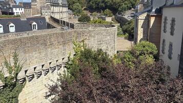 Un mur de pierre ancien, doté de créneaux, entouré de bâtiments et de verdure.
