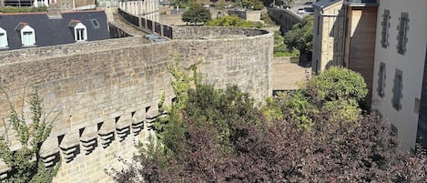 A historic stone wall with battlements, surrounded by buildings and greenery.