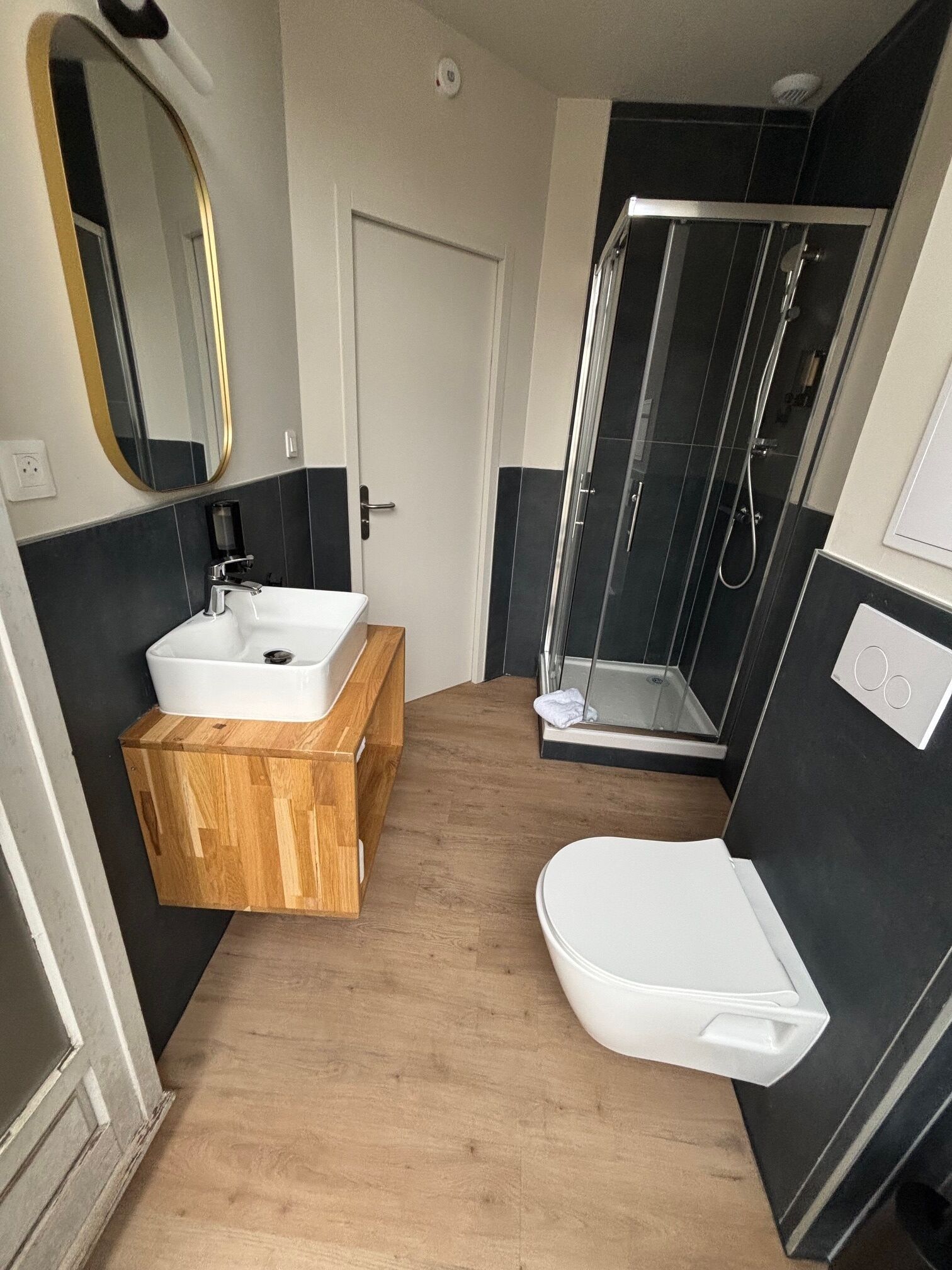 A modern bathroom with a wooden vanity, a white sink, a toilet, and a glass-enclosed shower.
