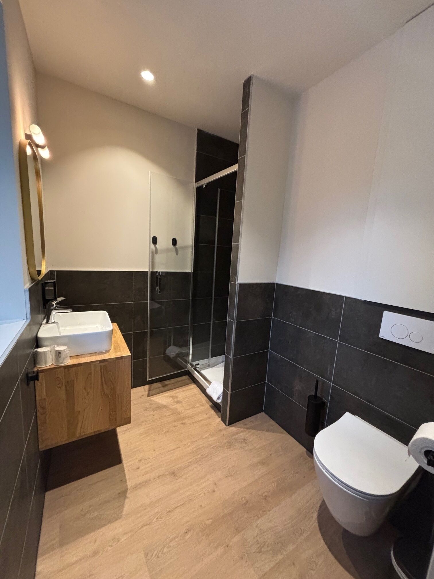 A modern bathroom with a wooden vanity, a white sink, a glass-enclosed shower, and a toilet.