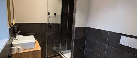 A modern bathroom with a wooden vanity, a white sink, a glass-enclosed shower, and a toilet.