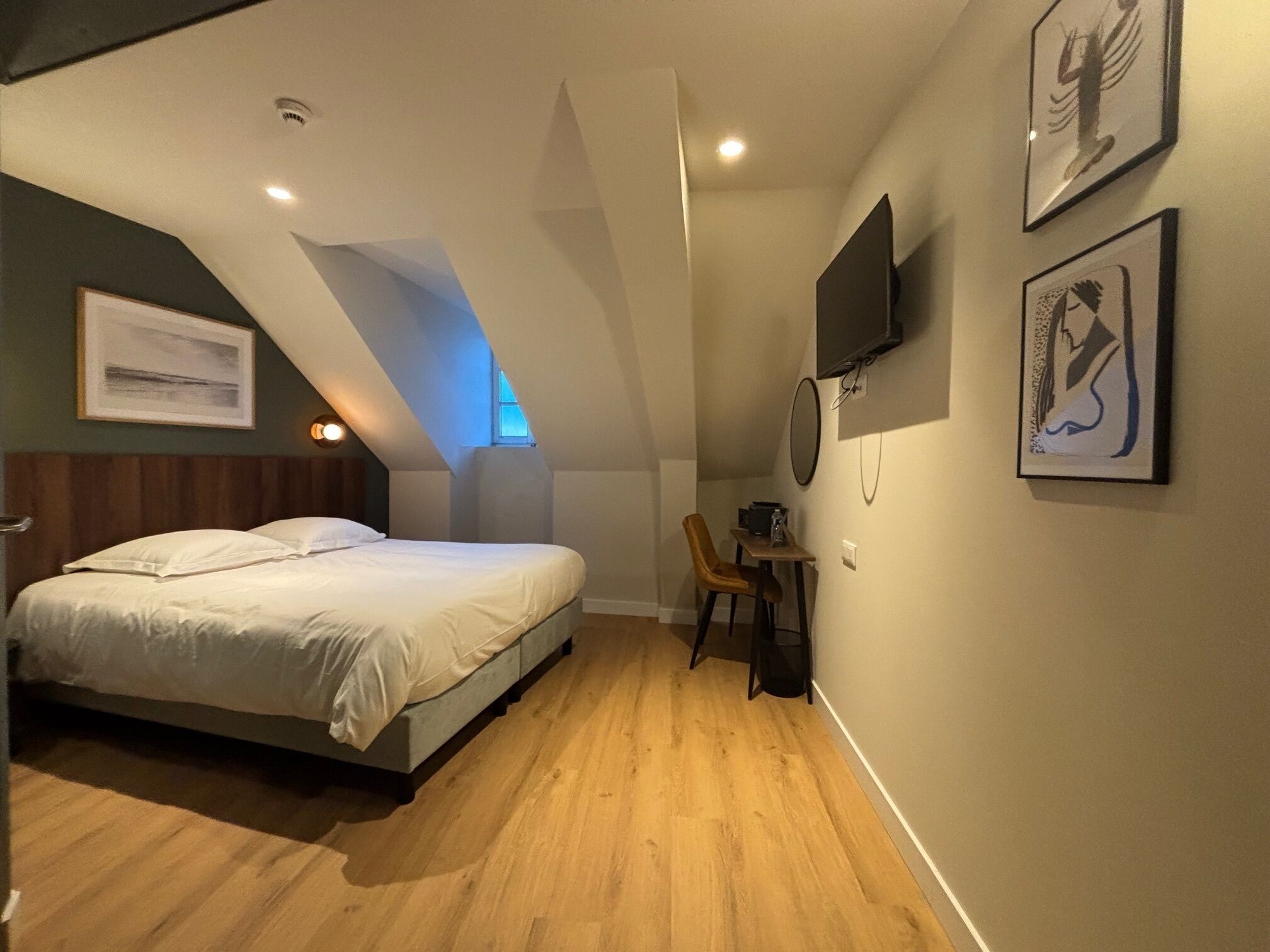 A bedroom with a bed, a desk, a chair, a TV, and artwork on the wall.