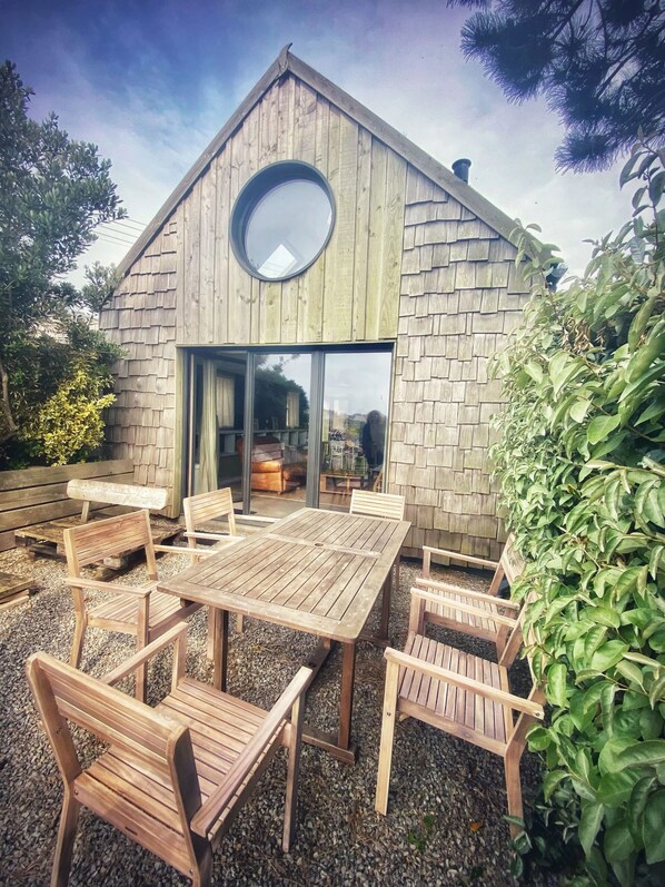 A wooden building with a circular skylight, large glass doors, and a patio with wooden furniture. - EMBRUNS D'HERBE SLOW CAMP (Plogoff)