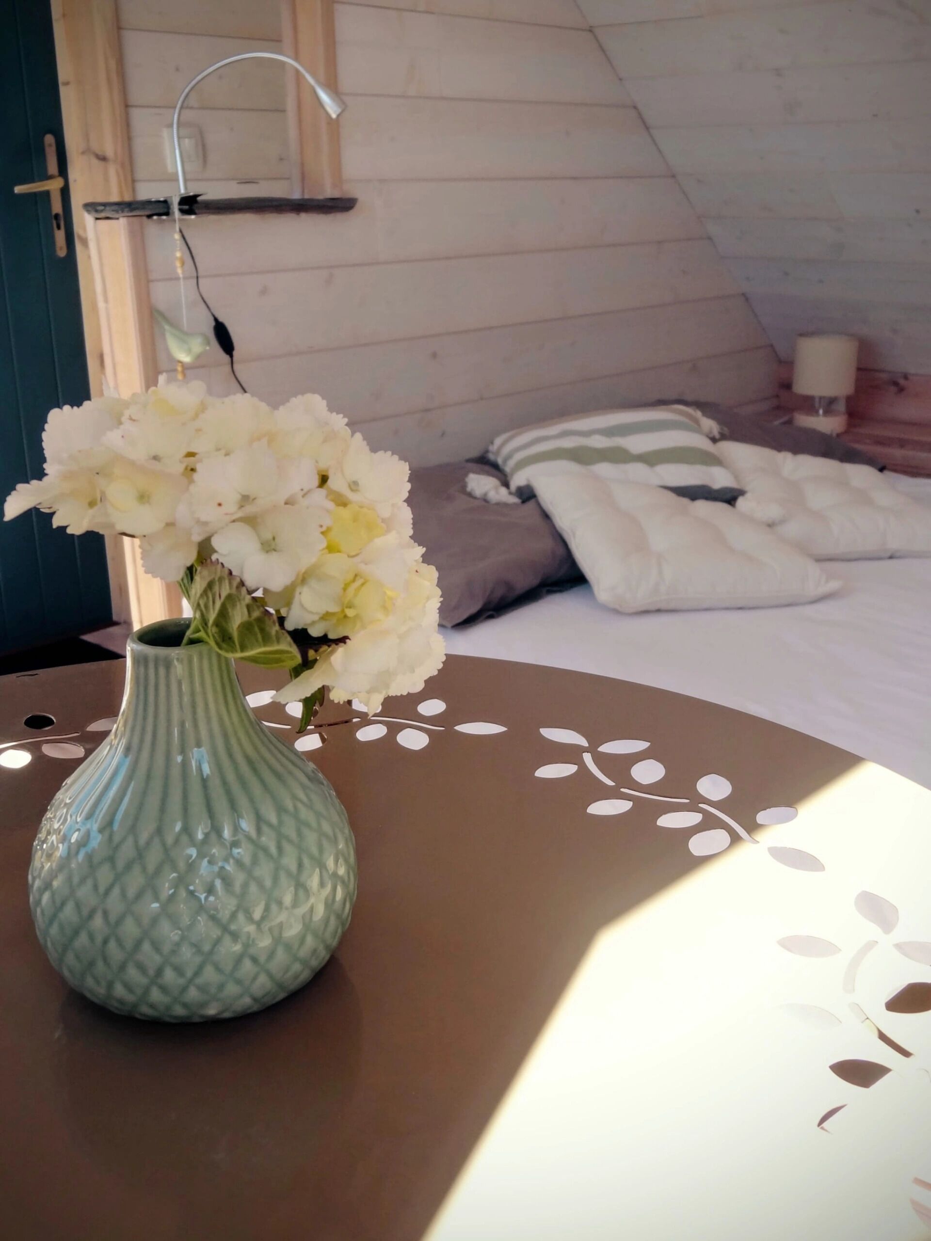 Une chambre avec un lit, une table de chevet ornée d’un vase de fleurs et une lampe fixée au mur.